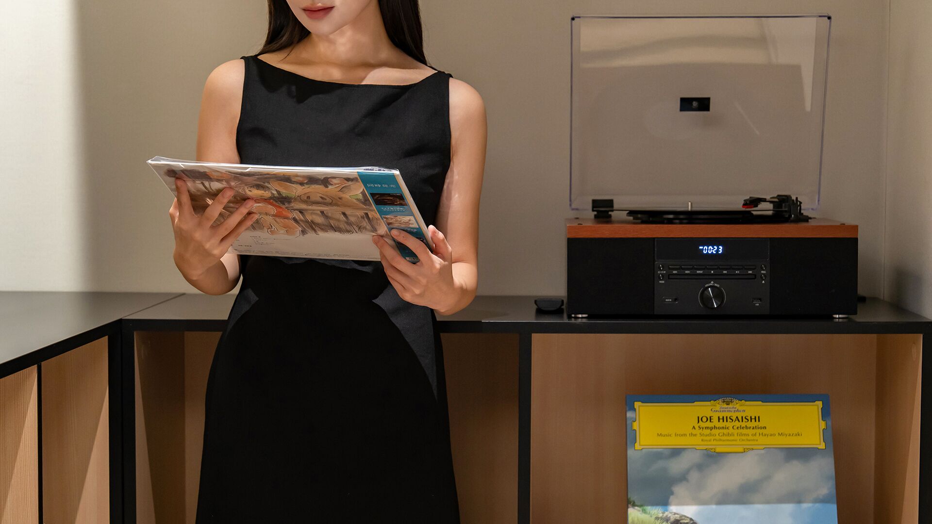 A person holding a magazine in a room with a wooden desk, a radio, and a poster on the wall.