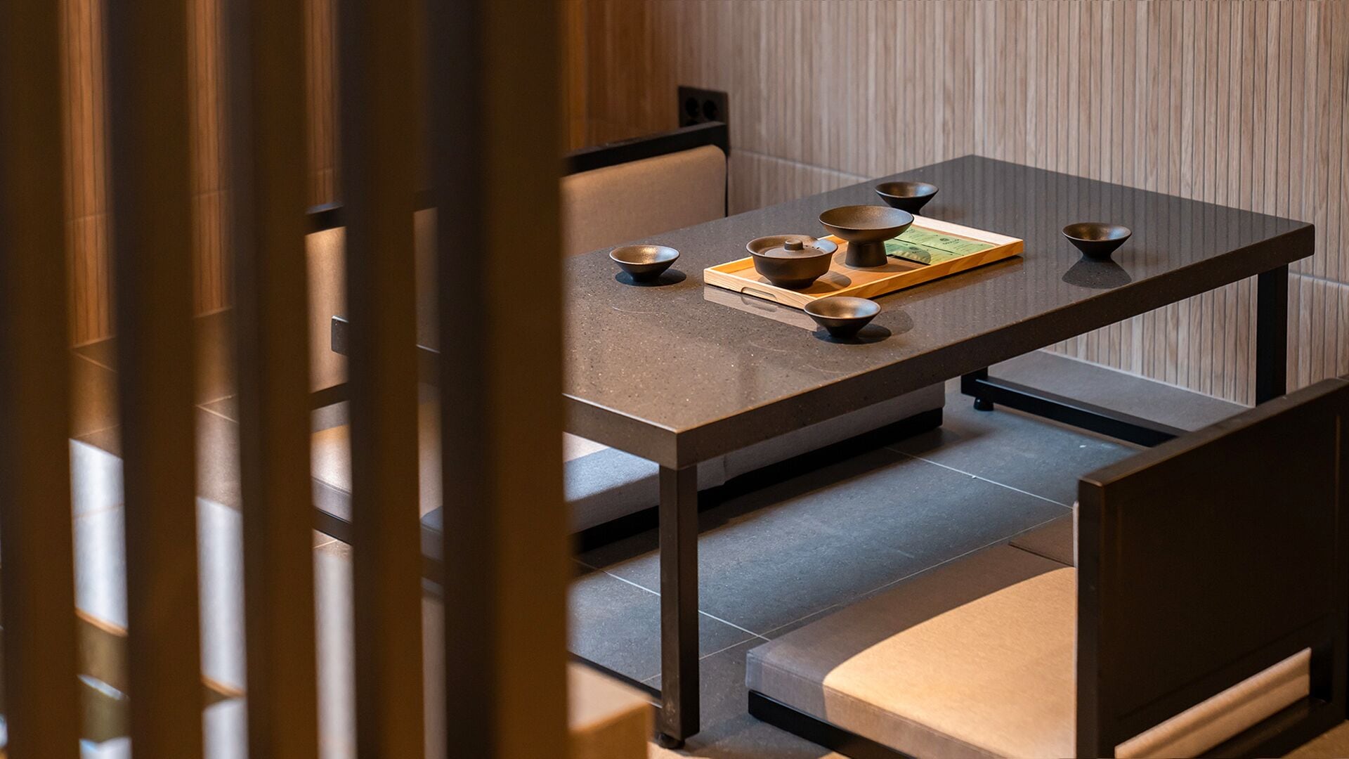 A minimalist dining area with a table set for two, featuring a wooden tray and traditional bowls.