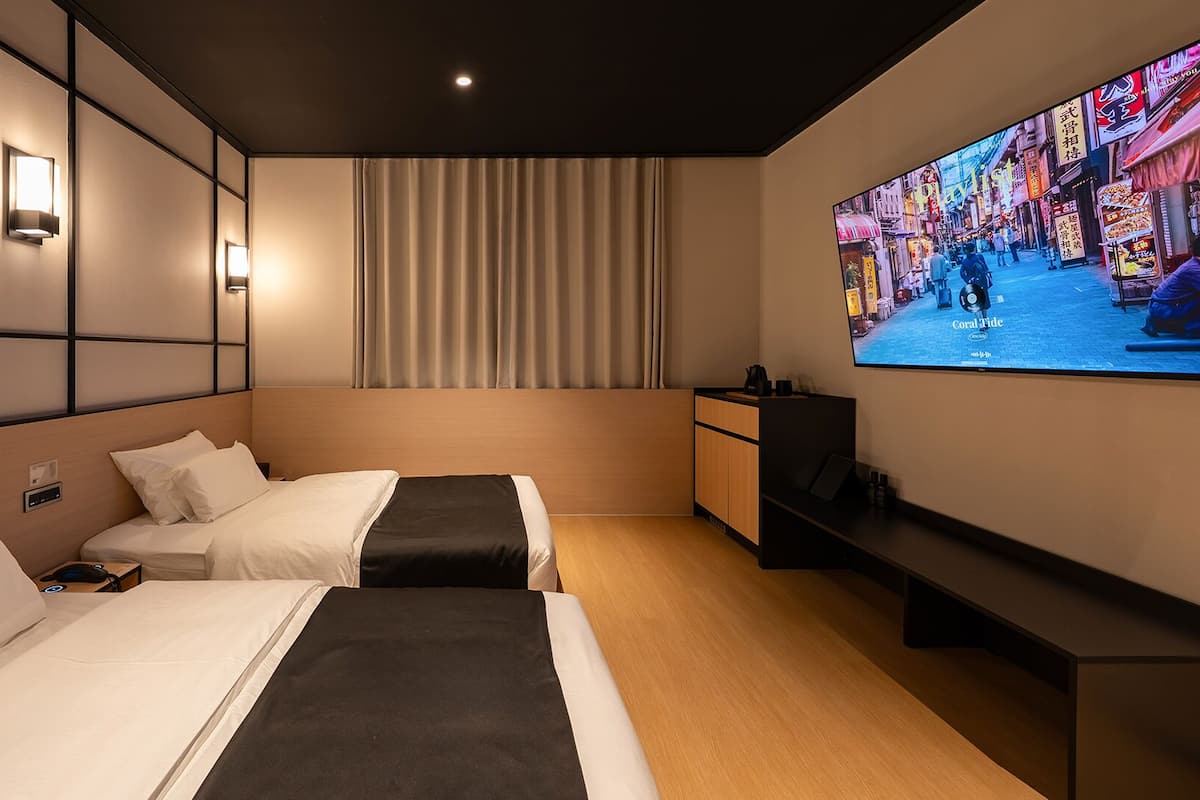 Ett hotellrum med två sängar, en TV och ett stort fönster med gardiner.