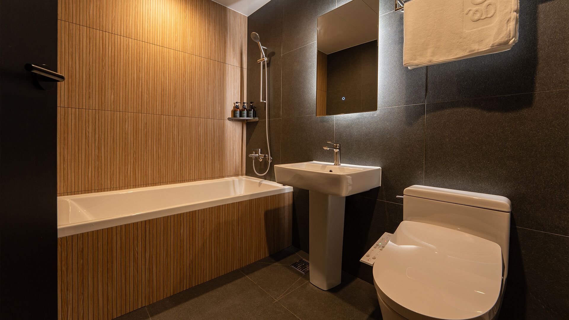 Et moderne badeværelse med en træpanelfag, et hvidt badekar, et konsolbord med vask og et toilet.