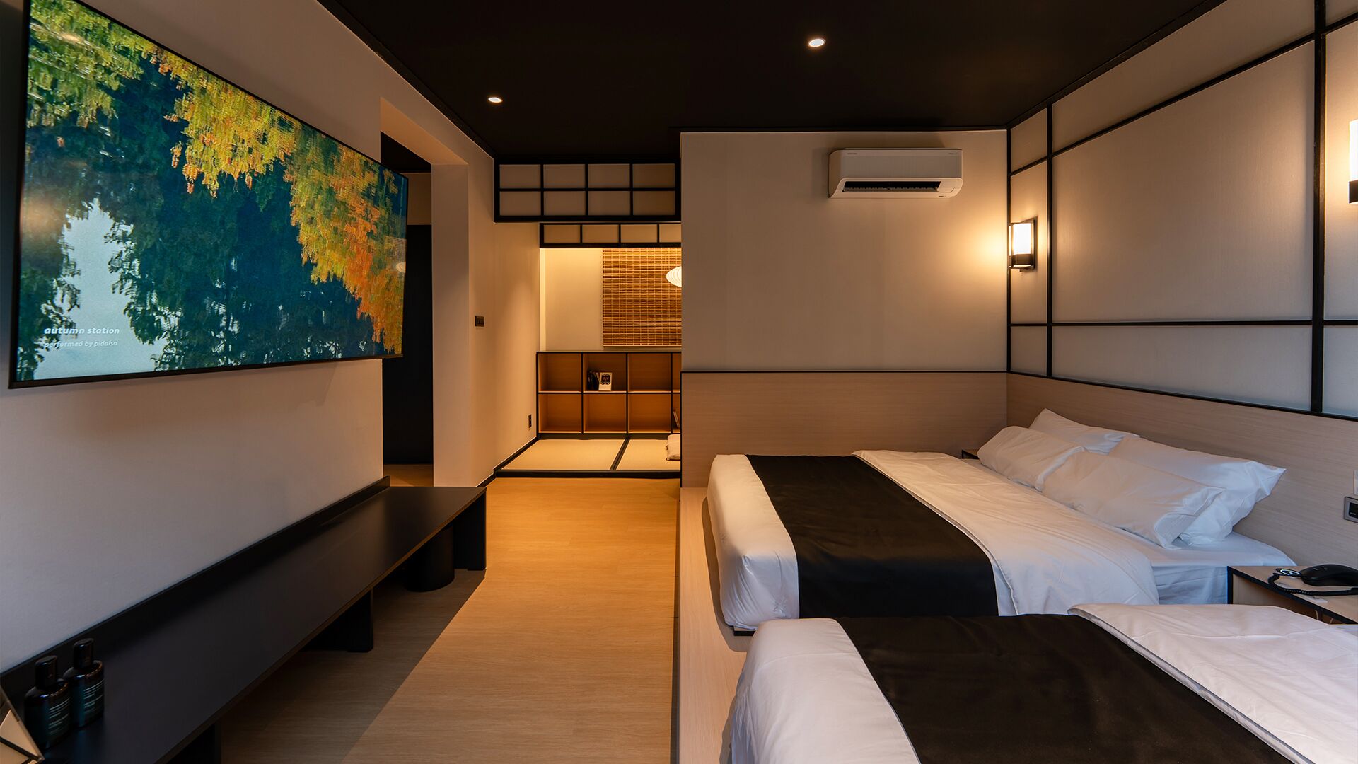 Habitación de hotel moderna con dos camas, un cuadro abstracto grande, un banco empotrado y una pequeña zona de estar con una mesa.