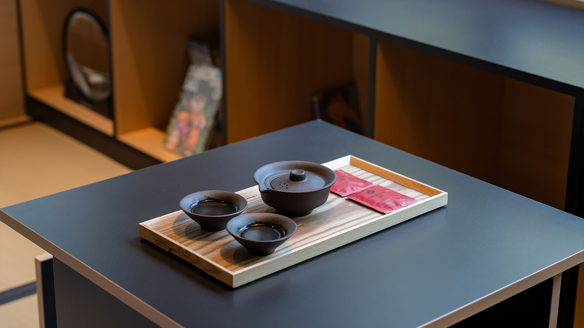 A table with three black bowls and a tray with a red packet on a wooden board.