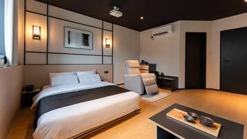 A modern hotel room with a large bed, a massage chair, a small table with bowls, and a projector on the ceiling.