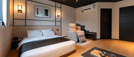 A modern hotel room with a large bed, a massage chair, a small table with bowls, and a projector on the ceiling.