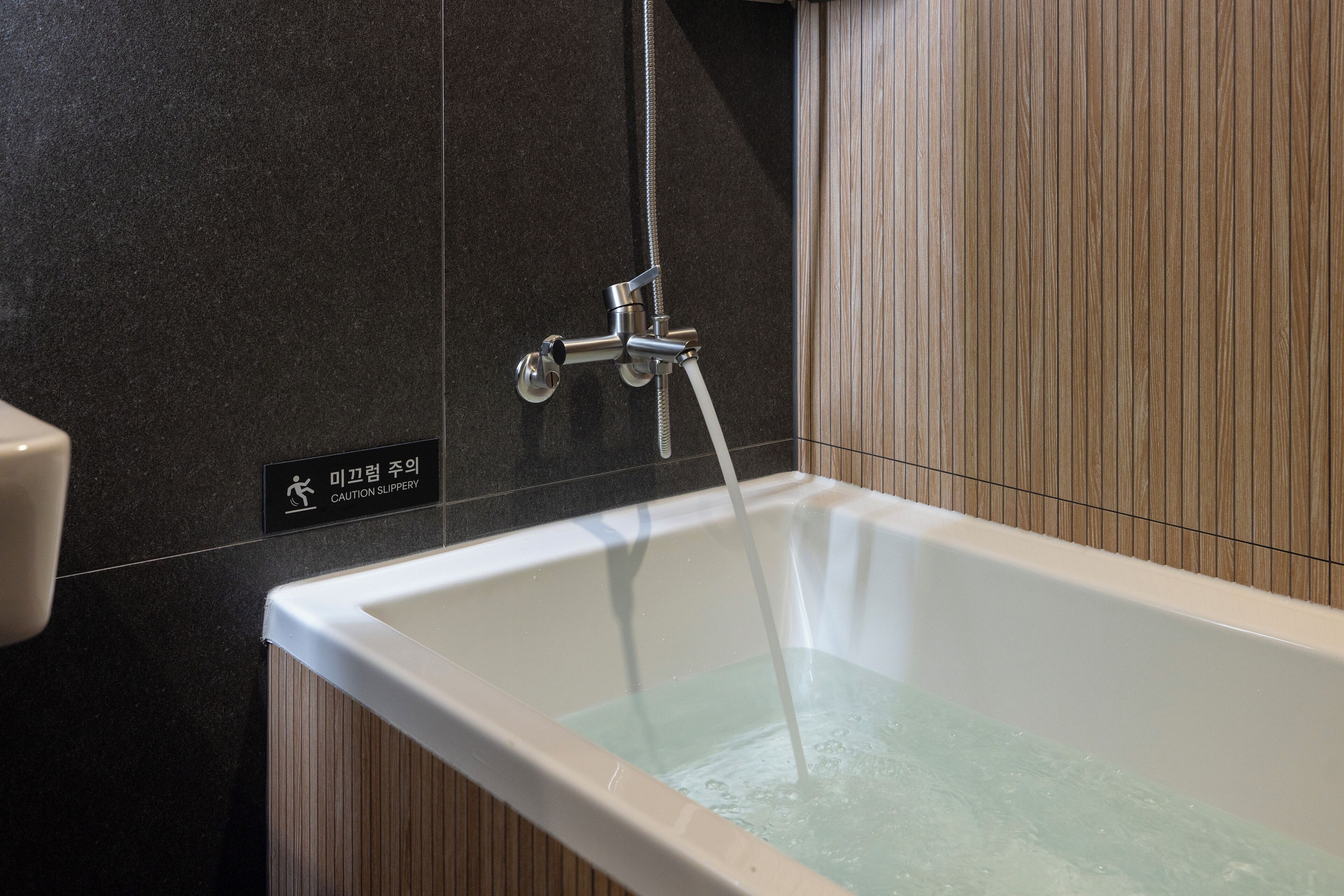 A modern bathroom with a bathtub, a showerhead, and a caution sign.