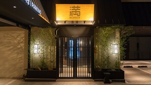 A hotel entrance with a modern design, featuring a large illuminated sign, a gated entrance, and potted plants. - Mitasuya Ryokan Hotel by Anook Gongju  (Gongju)