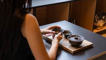 A person holding a small bowl on a wooden tray with a larger bowl and a pot on a table.
