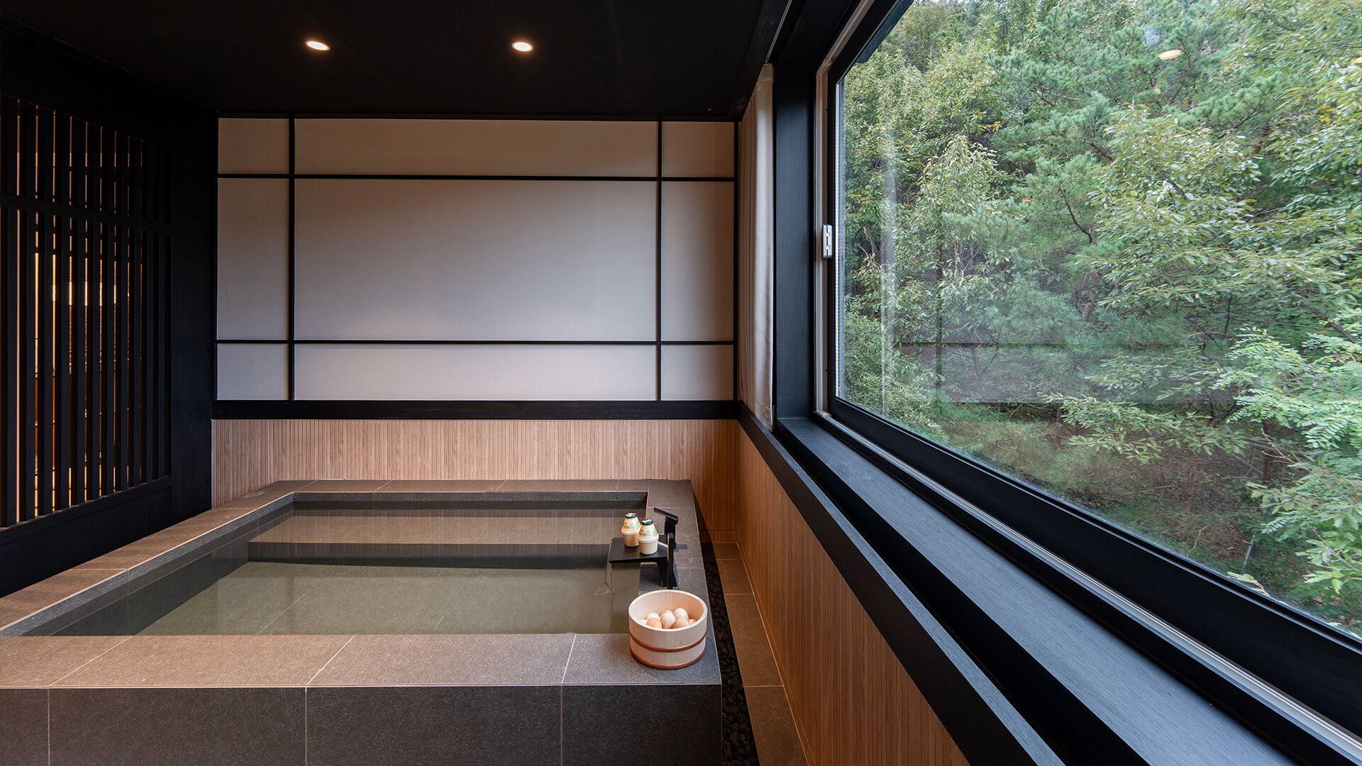 Un baño moderno con una bañera grande, paneles de madera y vistas a un bosque a través de un ventanal amplio.