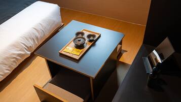 A neatly made bed with a white pillow and a wooden nightstand beside it. On the nightstand, there is a tray with a teapot, two cups, and a tea bag.