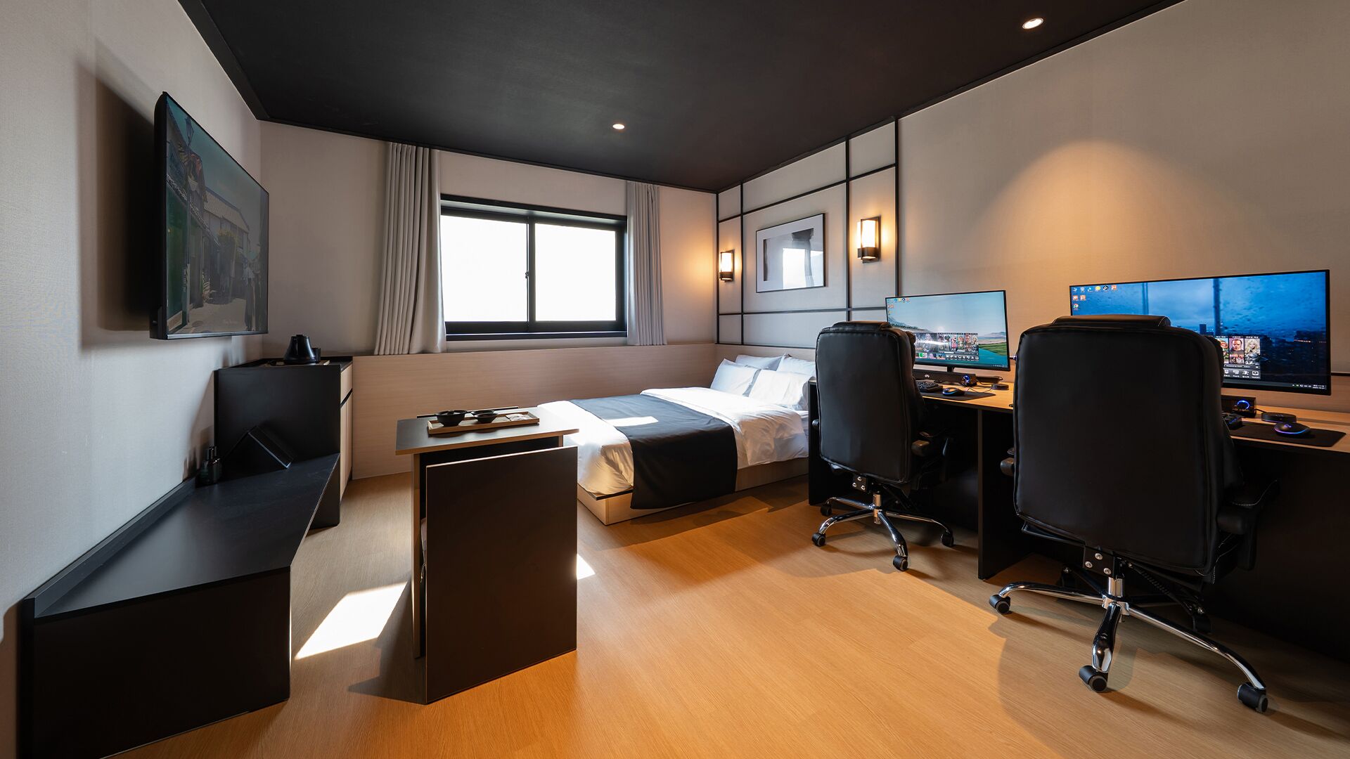 Ein modernes Hotelzimmer mit Bett, Schreibtisch, zwei Stühlen, einem Computerarbeitsplatz und einem großen Fenster.