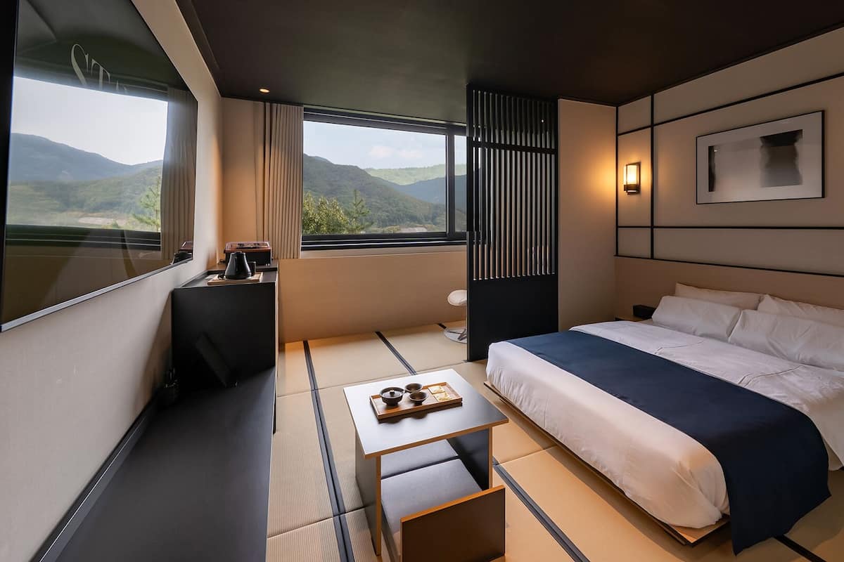 Ett modernt hotellrum med en stor säng, ett skrivbord, utsikt över bergen och en skjutdörr.