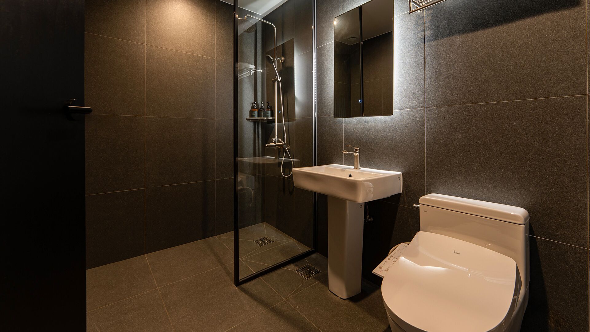 A modern bathroom with a glass-enclosed shower, a pedestal sink, and a toilet.
