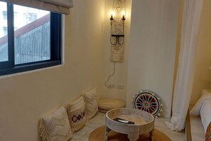 A room with a window, a wall-mounted light fixture, a round table, and a decorative wheel.