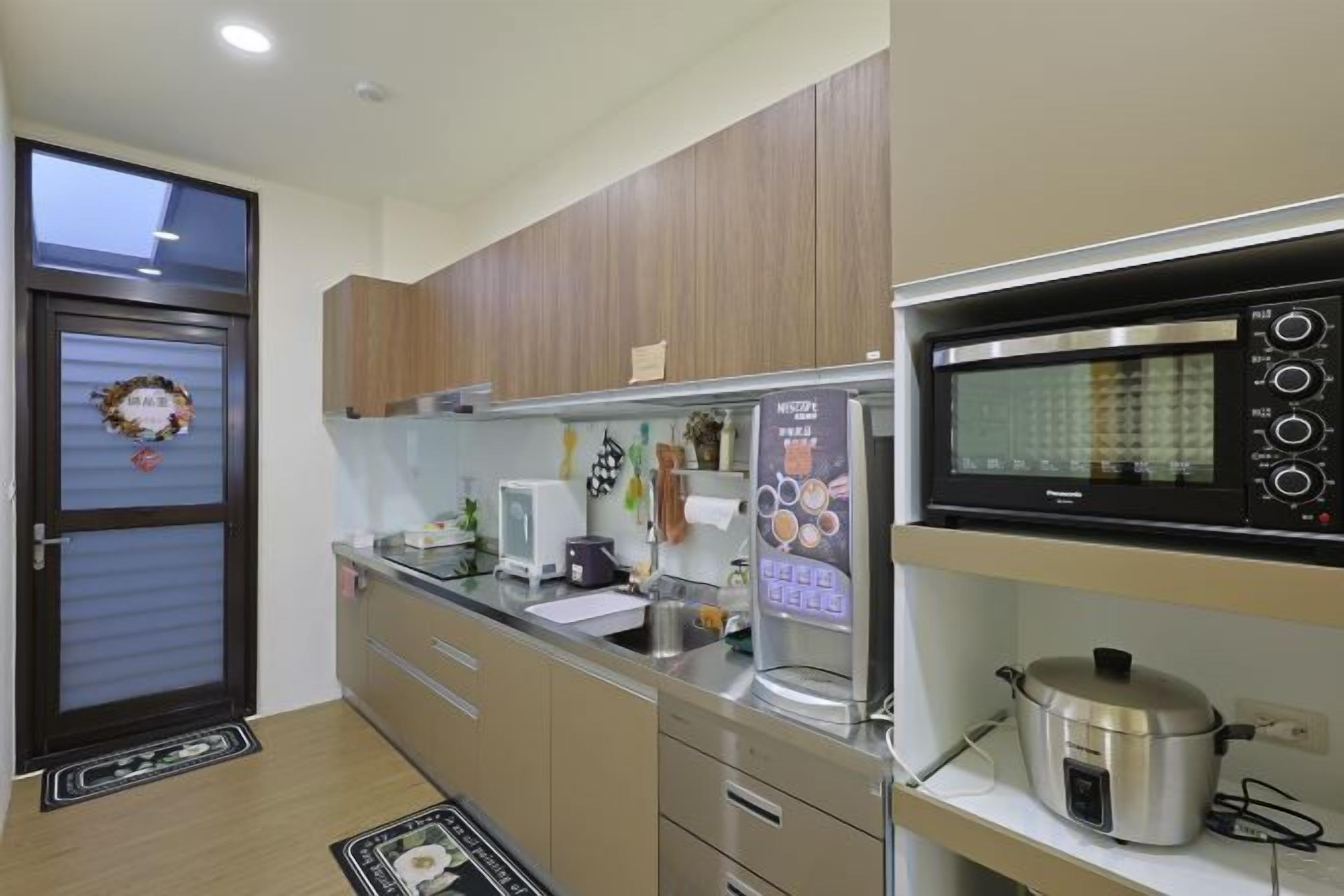 A kitchen with wooden cabinets, a microwave, a kettle, and a refrigerator.