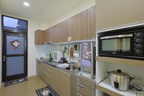 A kitchen with wooden cabinets, a microwave, a kettle, and a refrigerator. - Bubbleforest (Taitung)