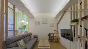 Ein modernes Wohnzimmer mit grauem Sofa, Couchtisch aus Holz und Fernseher an einer weißen Wand.