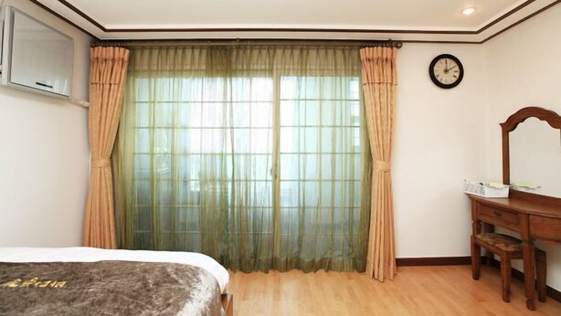 A bedroom with a bed, a wooden desk, a mirror, and a window with sheer curtains. - seaview (Jeju)