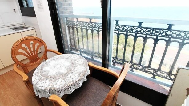 Une petite cuisine avec une fenêtre, une chaise en bois et une table recouverte d’une nappe en dentelle.