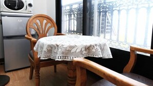 A dining area with a table covered by a white lace tablecloth, a wooden chair, and a view of a bridge through a window. - seaview (Jeju)
