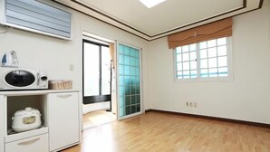 A room with a wooden floor, a microwave, a small refrigerator, a sliding glass door, and a window with blinds. - seaview (Jeju)