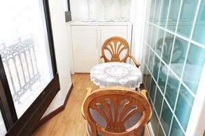 A corner room with a wooden chair, a small round table with a lace tablecloth, a white wardrobe, and a window with a view of a building. - seaview (Jeju)