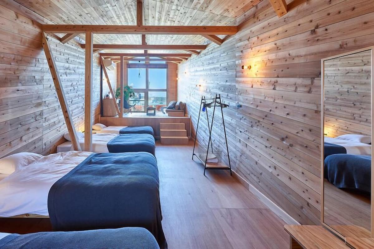 Una cabaña con paredes de madera, una escalera central y una cama con colcha azul.