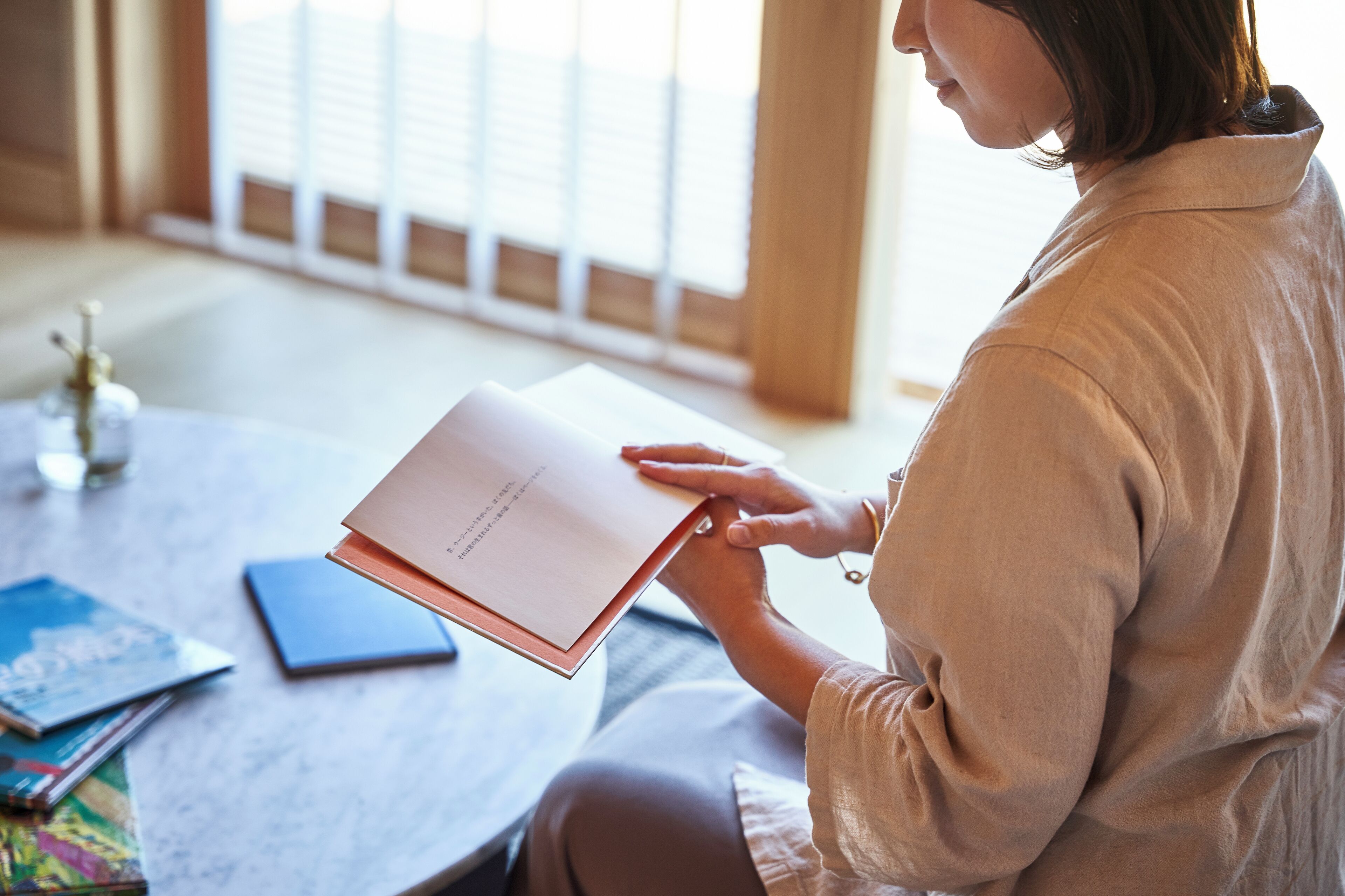 A person sitting at a table with a book, a blue notebook, and a pen.