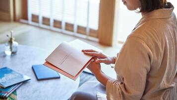 A person sitting at a table with a book, a blue notebook, and a pen.