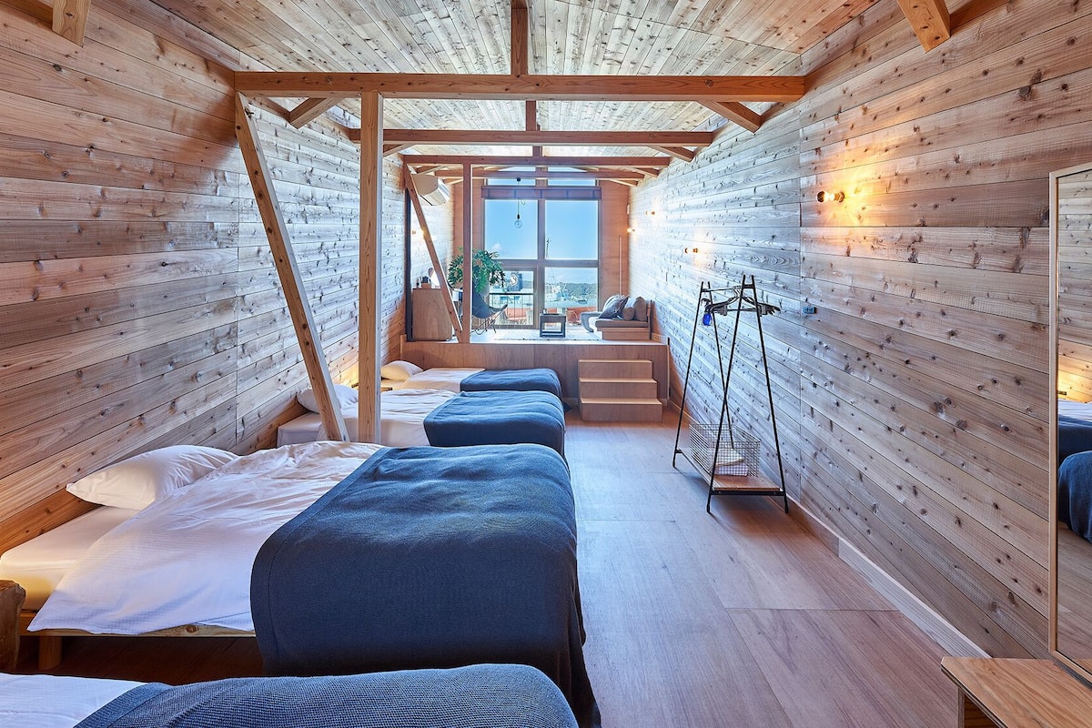 Una cabaña de madera con literas, un pequeño rincón de descanso y un ventanal grande.