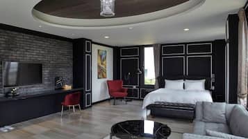 A modern hotel room with a large bed, a TV, a red chair, a sofa, and a unique ceiling design.