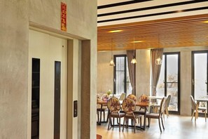 A dining area with tables and chairs, a wooden ceiling, and a view through a glass door.