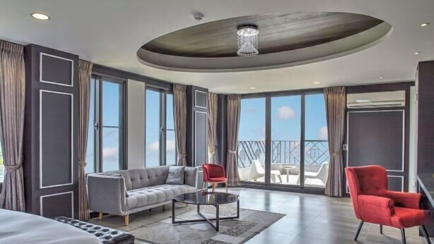 A modern hotel room with a large bed, a grey sofa, a red armchair, a glass coffee table, and a balcony with a view. - Lafika｜Dao Villa (Yilan)