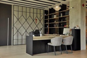 A modern office space with a desk, two chairs, a bookshelf, and a decorative chandelier.