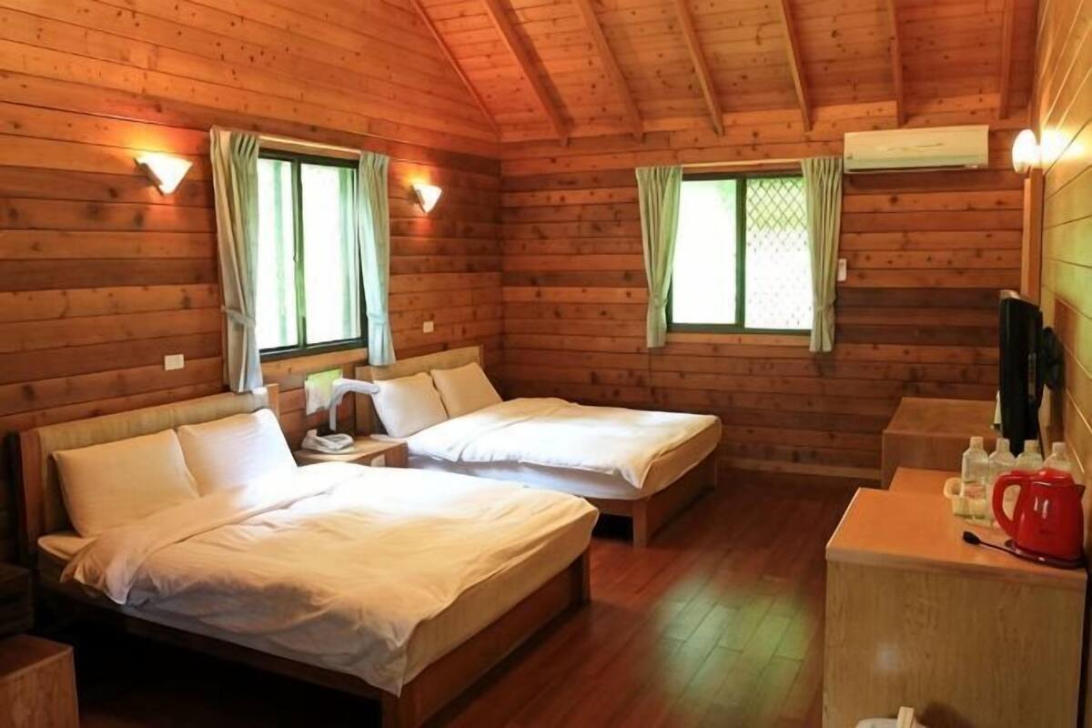A cabin with two beds, a small table, a red kettle, and wooden walls.