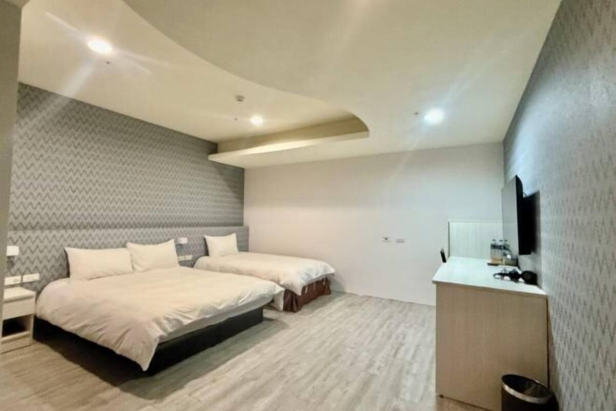 A modern bedroom with two beds, a small bedside table, a built-in desk, and a mirror.