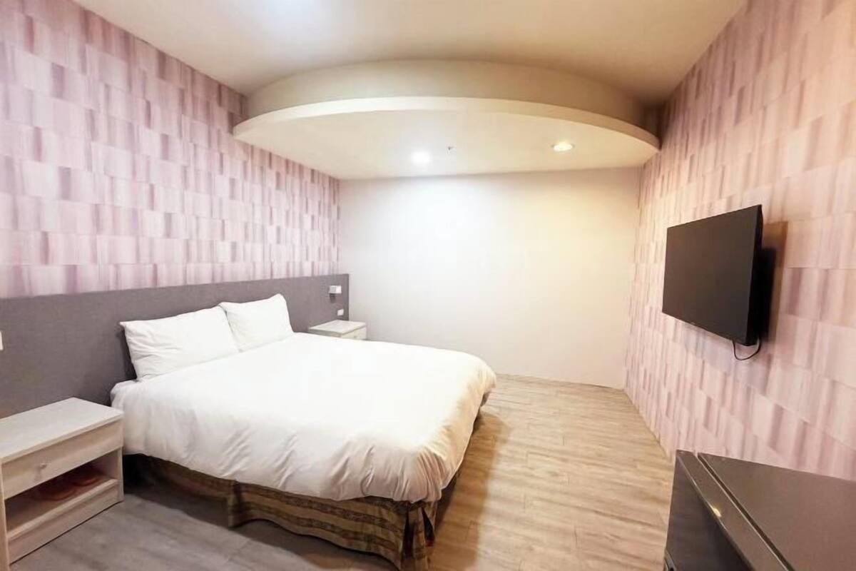 A modern bedroom with a bed, bedside table, TV, and a unique ceiling design.