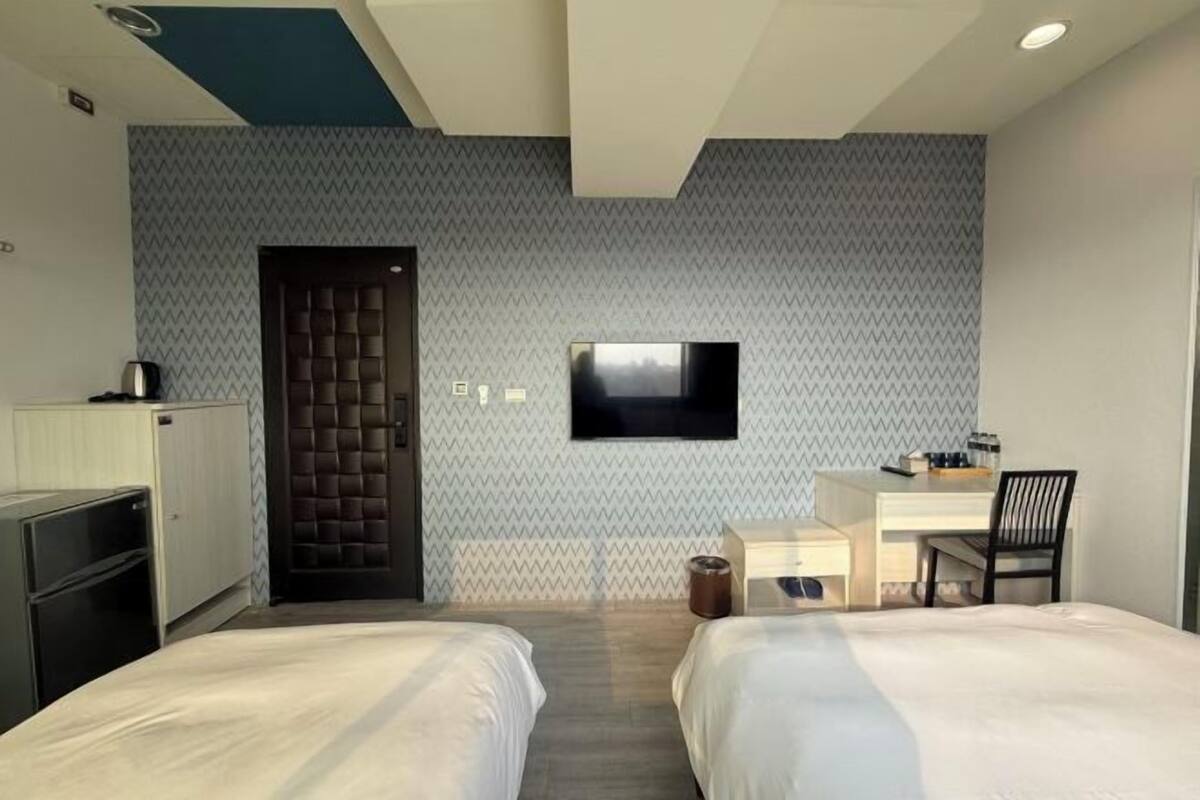 A hotel room with two beds, a desk, a TV, and a wardrobe.