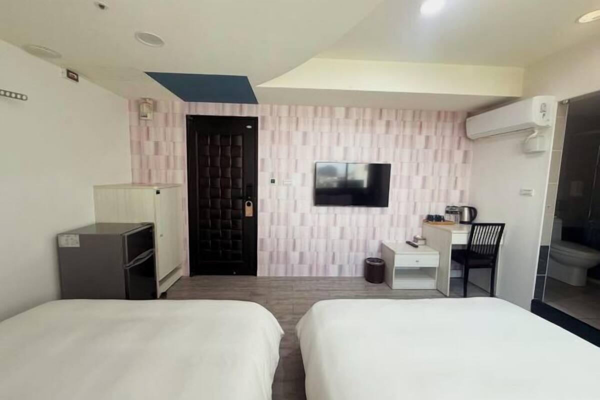 A hotel room with two beds, a desk, a chair, a TV, and a wardrobe.