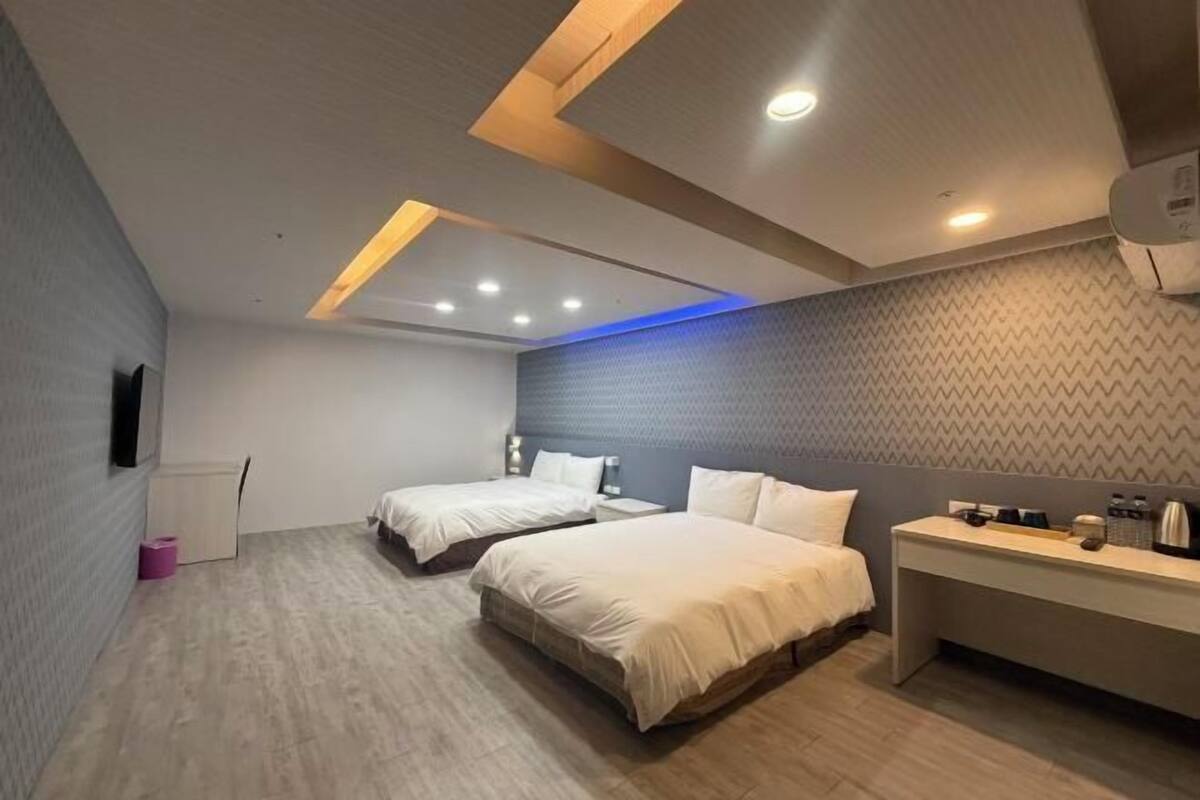 A modern hotel room with two beds, a desk, and a flat-screen TV.