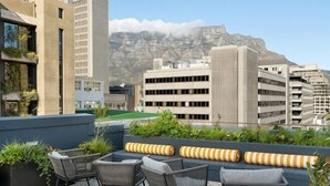 Une terrasse sur le toit, aménagée avec des espaces de détente en plein air, des plantes et offrant une vue sur les bâtiments de la ville et les montagnes.