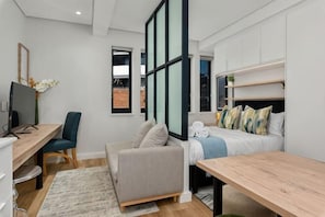 A modern hotel room with a bed, a desk, a chair, a sofa, and a TV. - The Carrington Aparthotel by Totalstay (Cape Town)