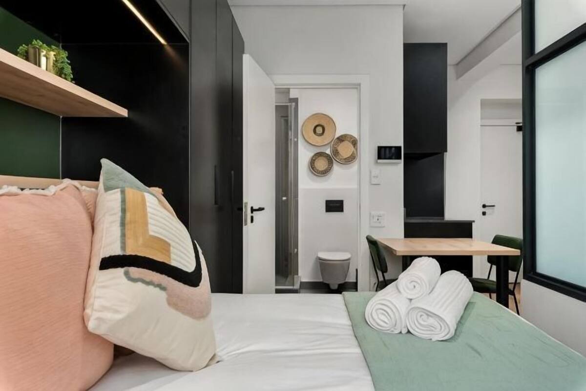 Ein modernes Hotelzimmer mit Bett, kleinem Tisch, Sessel und Blick auf den Flur.
