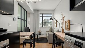 Un espace de vie compact comprenant un coin cuisine, un espace repas, un canapé et une grande fenêtre donnant sur la ville.