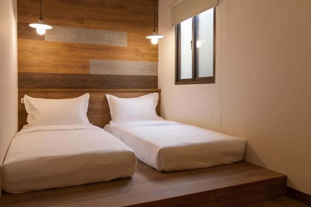 A small room with two beds, wooden paneling on the wall, and a window.