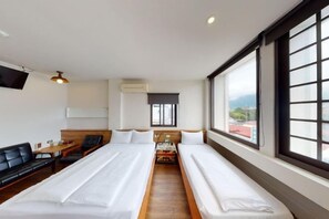 A hotel room with two beds, a sofa, a TV, and a window with a view. - Mini Voyage Hostel (Hualien)