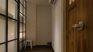 A narrow hallway with a wooden door, a white stool, and a trash bin. - Mini Voyage Hostel (Hualien)