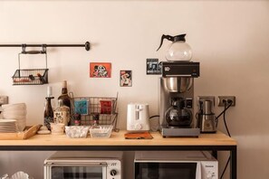 A kitchen area with a coffee machine, toaster, and microwave. There are various kitchen utensils and containers on the counter. - Mini Voyage Hostel (Hualien)