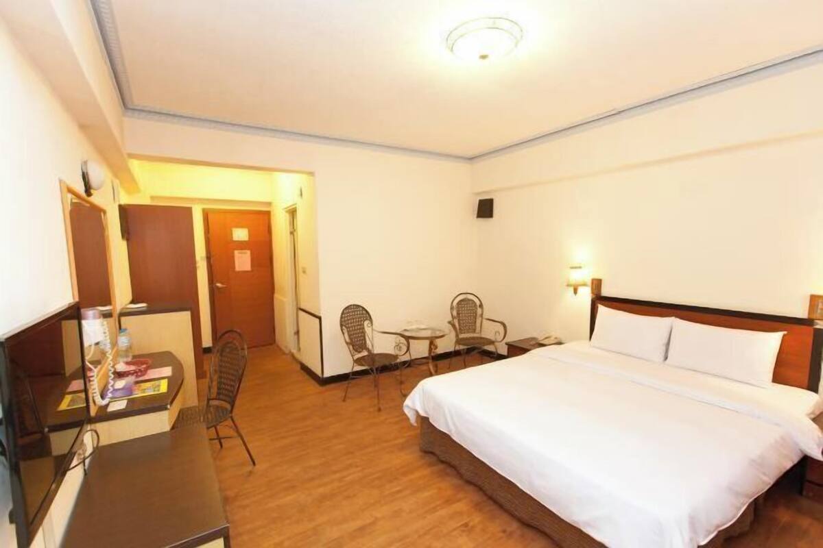 A hotel room with a bed, desk, chairs, and a small table.