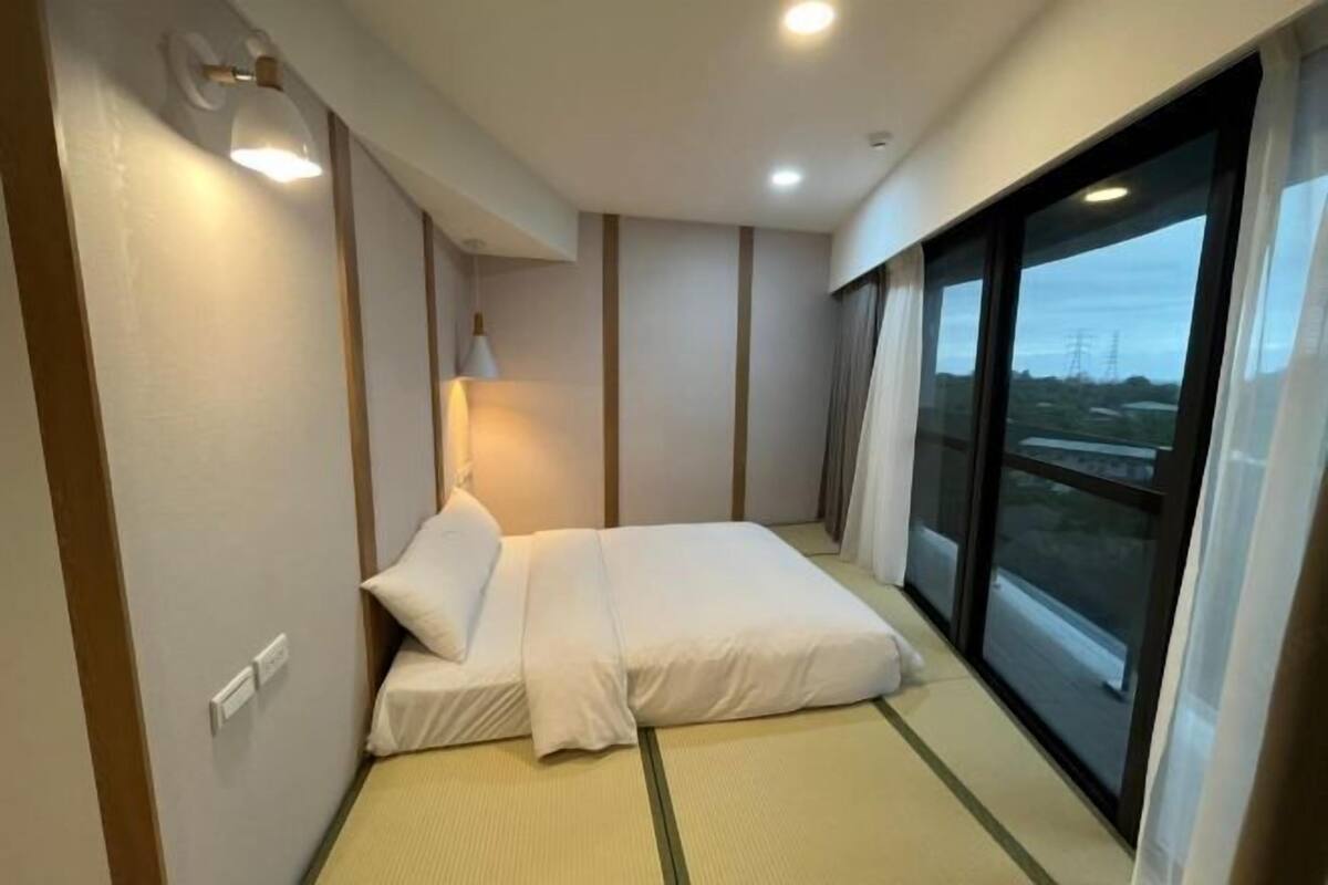 A hotel room with a bed, a lamp, a window, and a view of the outside.