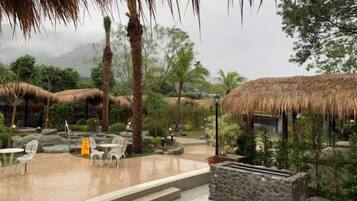 Un área de estar al aire libre con sombrillas de paja, muros de piedra y plantas tropicales.